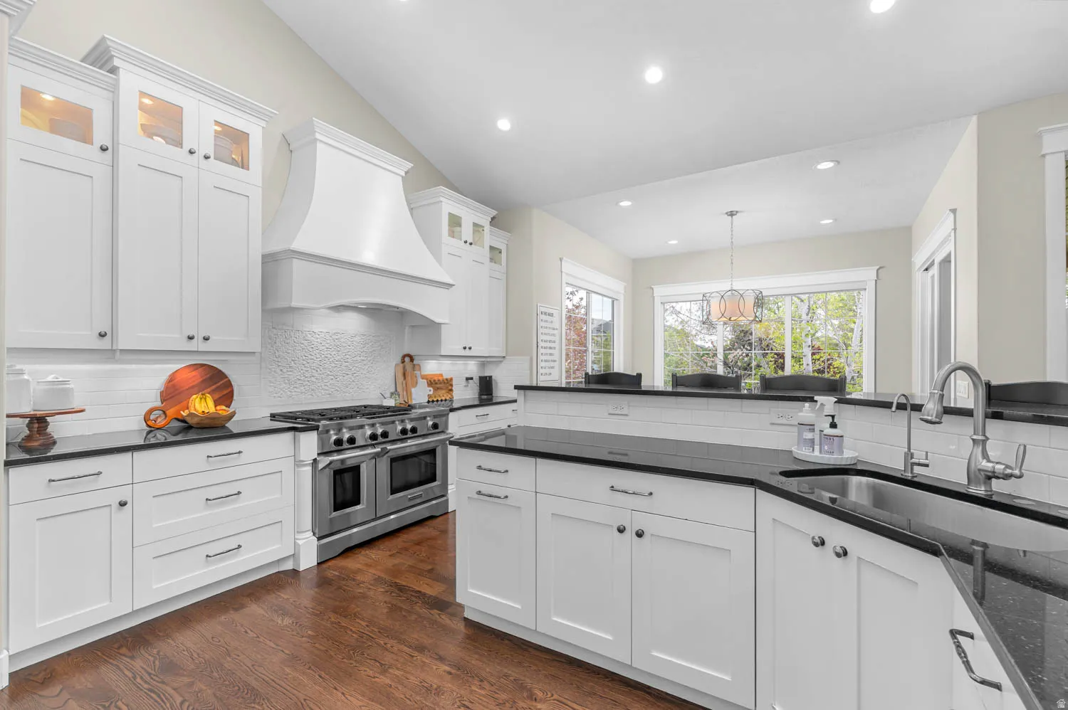 Kitchen featuring dark stone counters, double oven range, white cabinetry, glass fronted cabinets, and vaulted ceiling