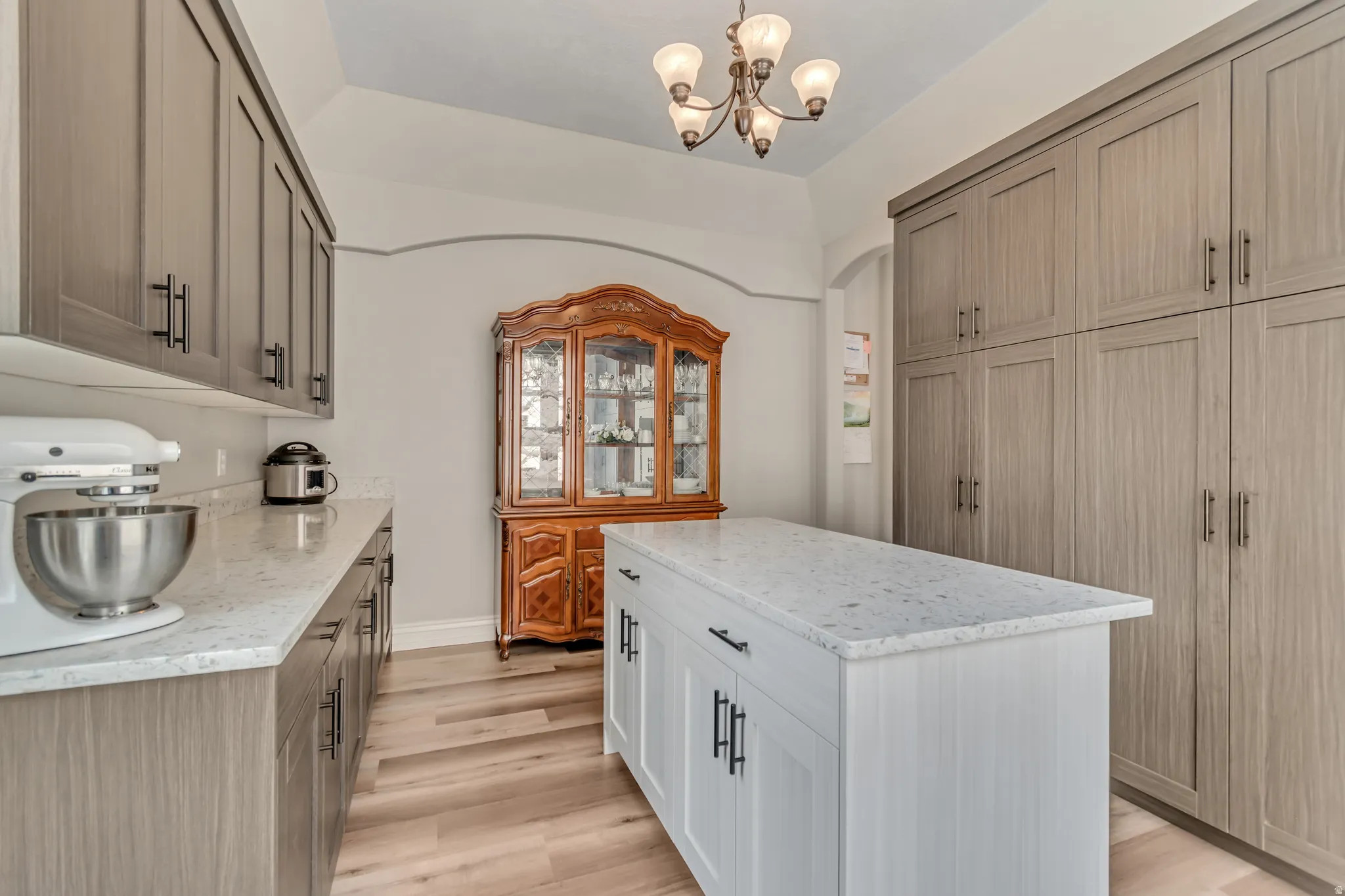 Dual tone kitchen featuring two tone cabinetry, light stone countertops, light wood-type flooring, a kitchen island, and hanging lights