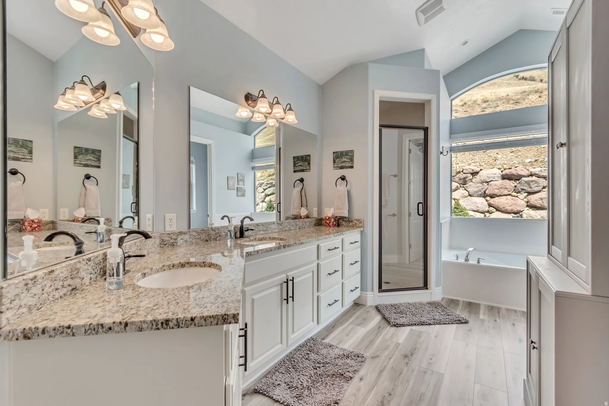 Bathroom with double vanity, a chandelier, vaulted ceiling, a garden tub, and healthy amount of natural light