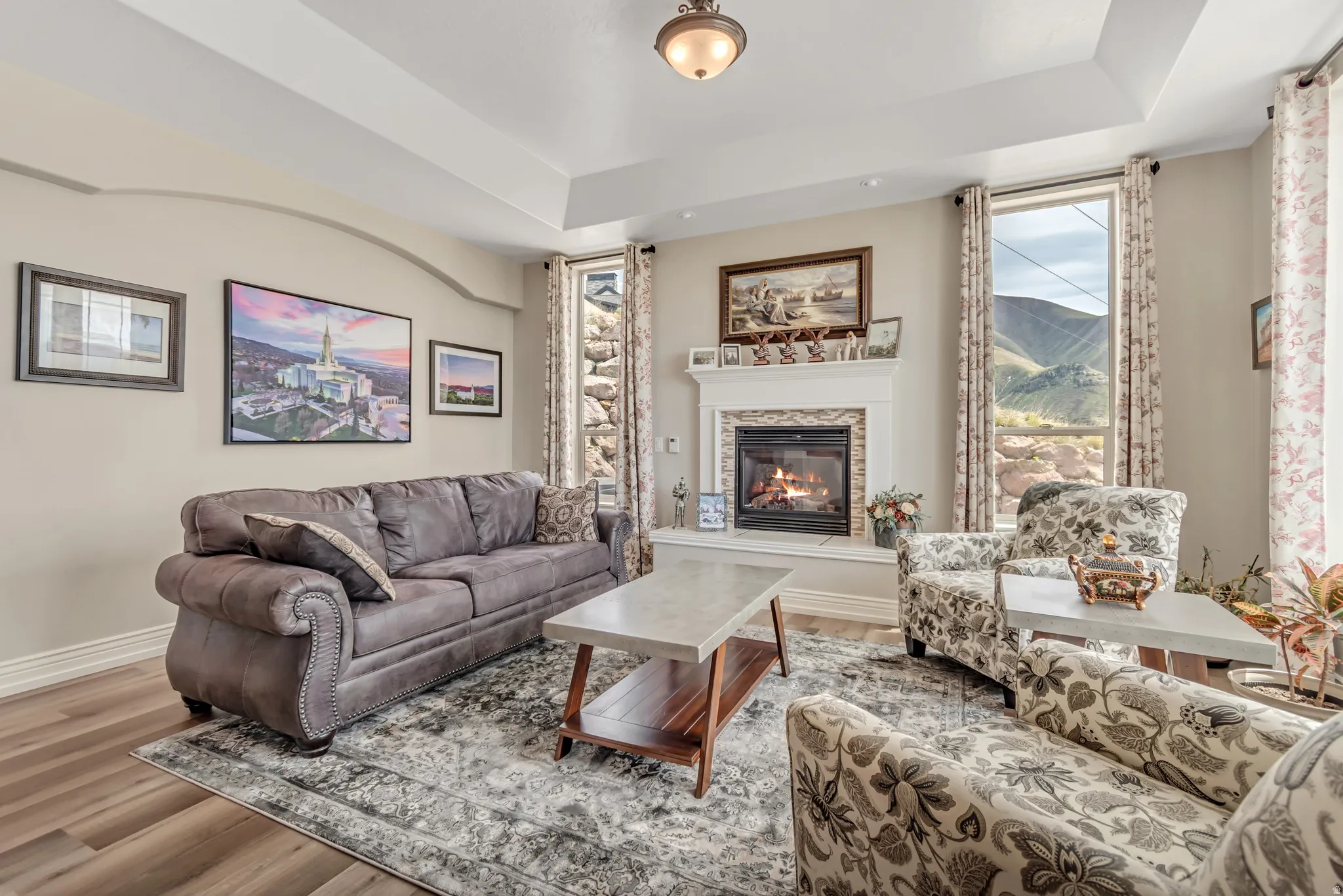 Living area with a raised ceiling, a glass covered fireplace, wood finished floors, and a mountain view