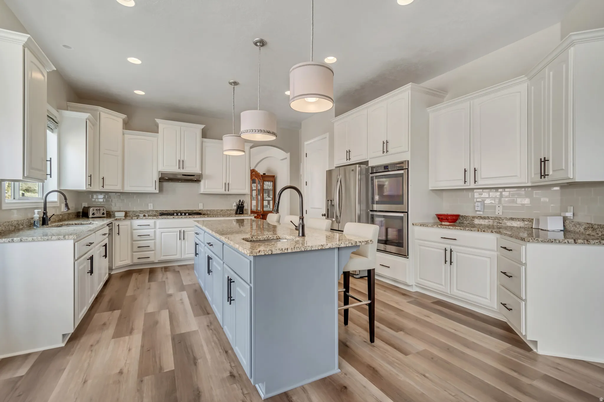 Two tone kitchen with decorative backsplash, hanging light fixtures, a kitchen breakfast bar, light stone counters, and light wood-type flooring
