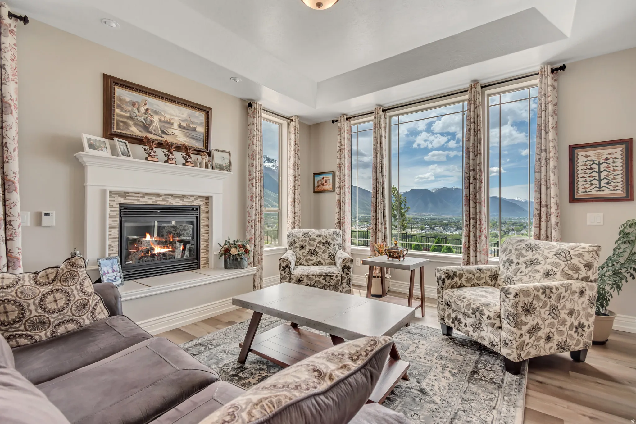 Living room with a mountain view, wood finished floors, a glass covered fireplace, and a tray ceiling