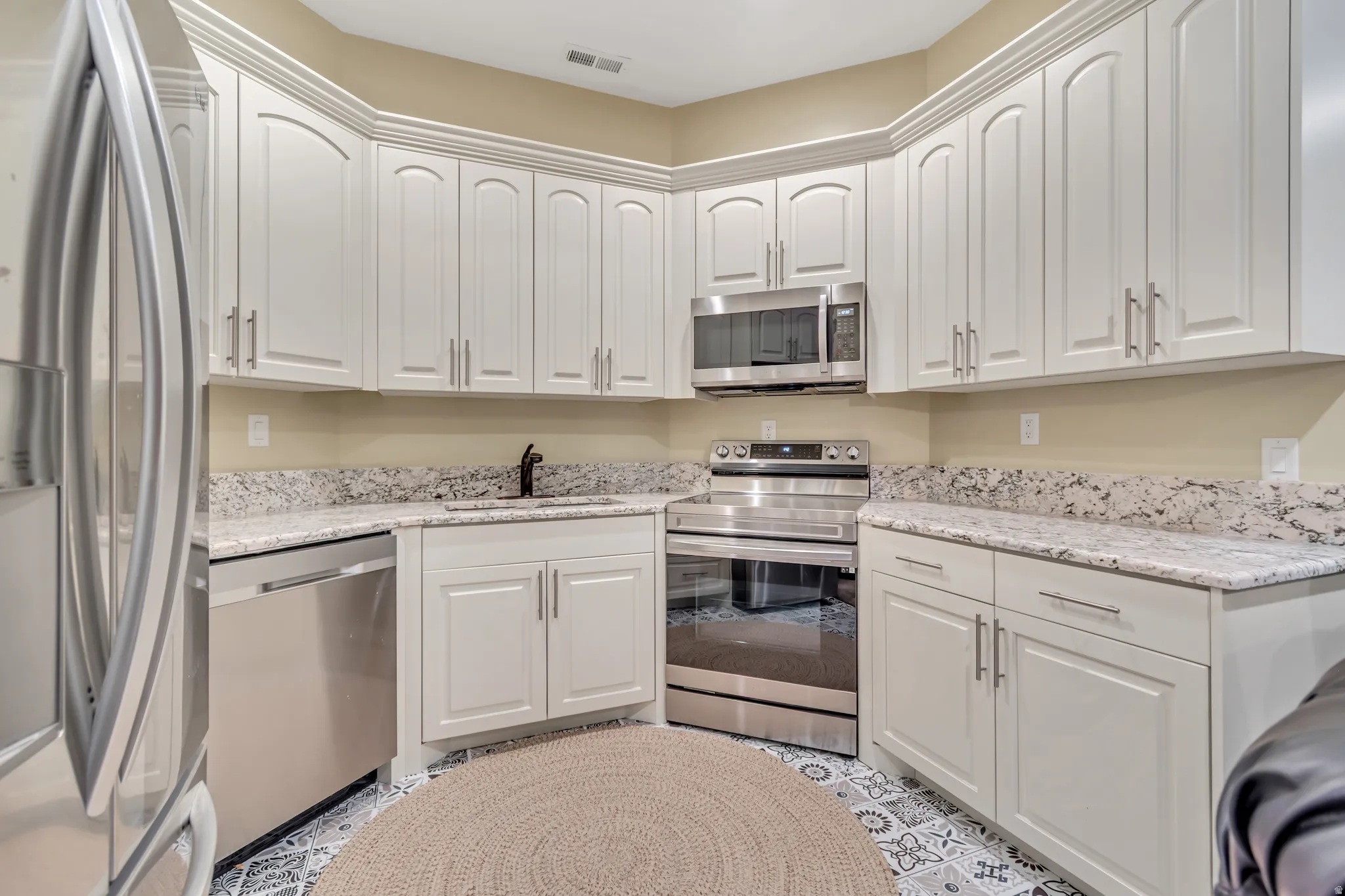 Kitchen with stainless steel appliances, light stone countertops, and white cabinets