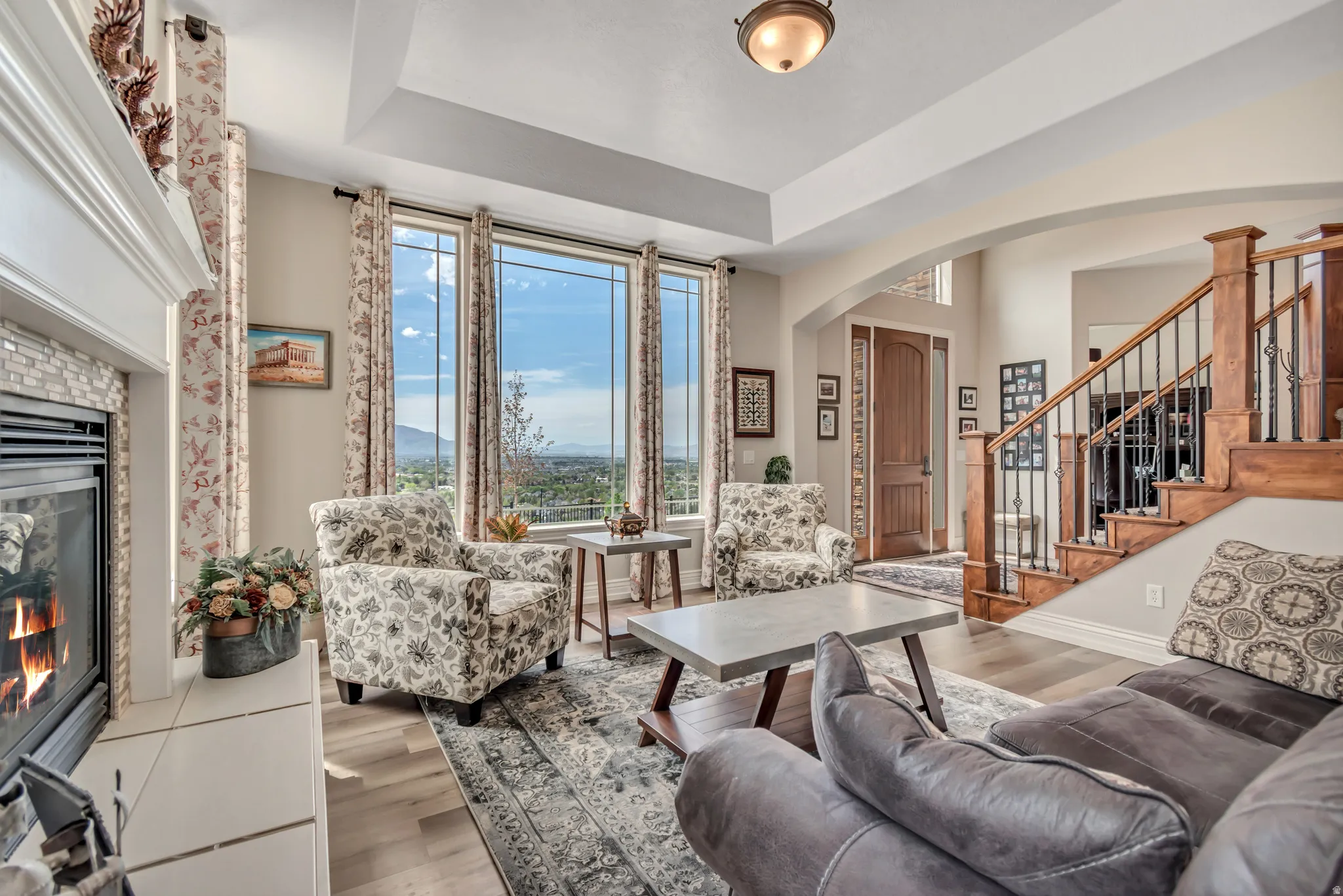 Living area featuring arched walkways, a glass covered fireplace, wood finished floors, and a tray ceiling