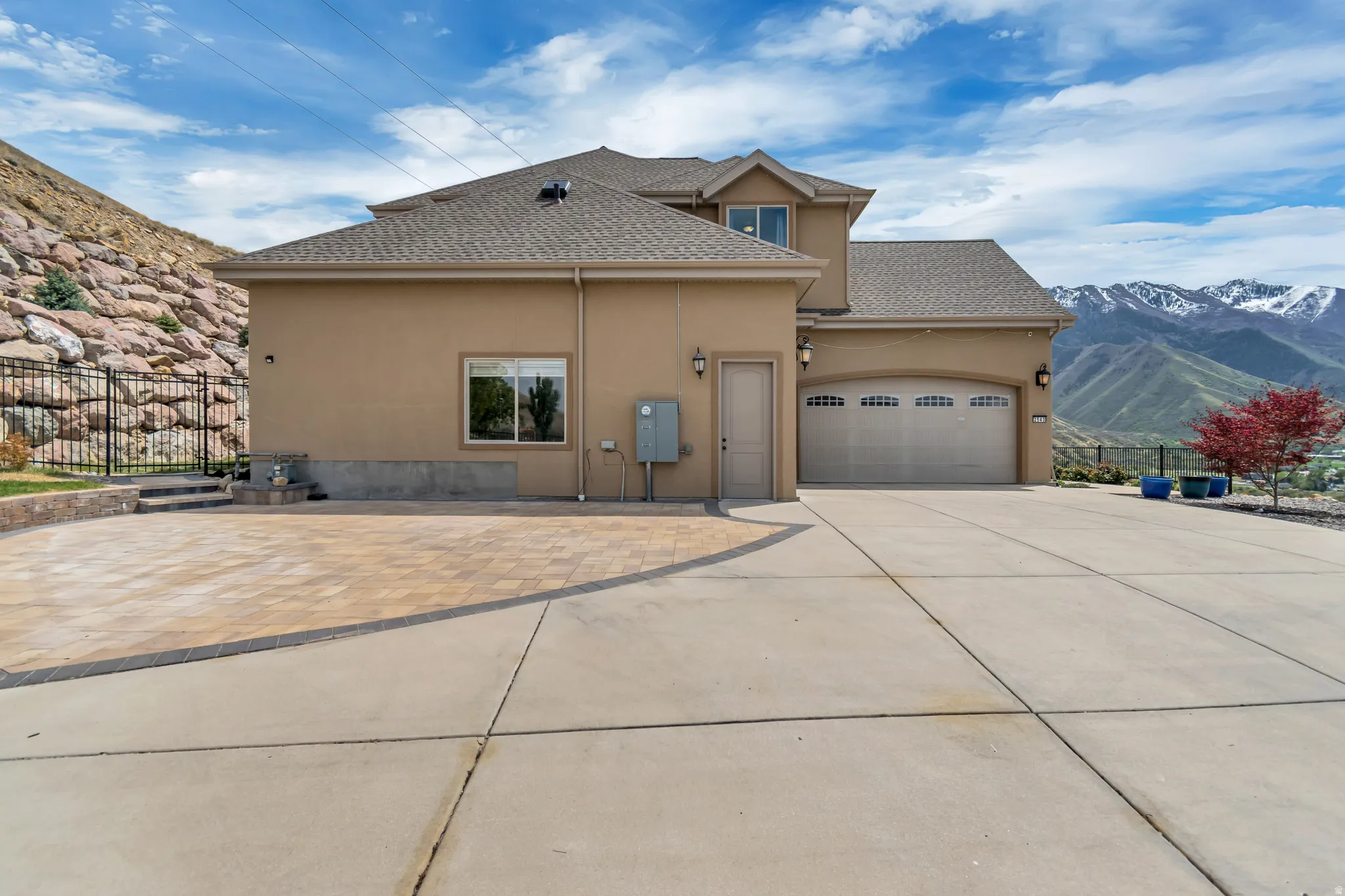 View of side of property featuring stucco siding, a garage, a mountain view, roof with shingles, and concrete driveway
