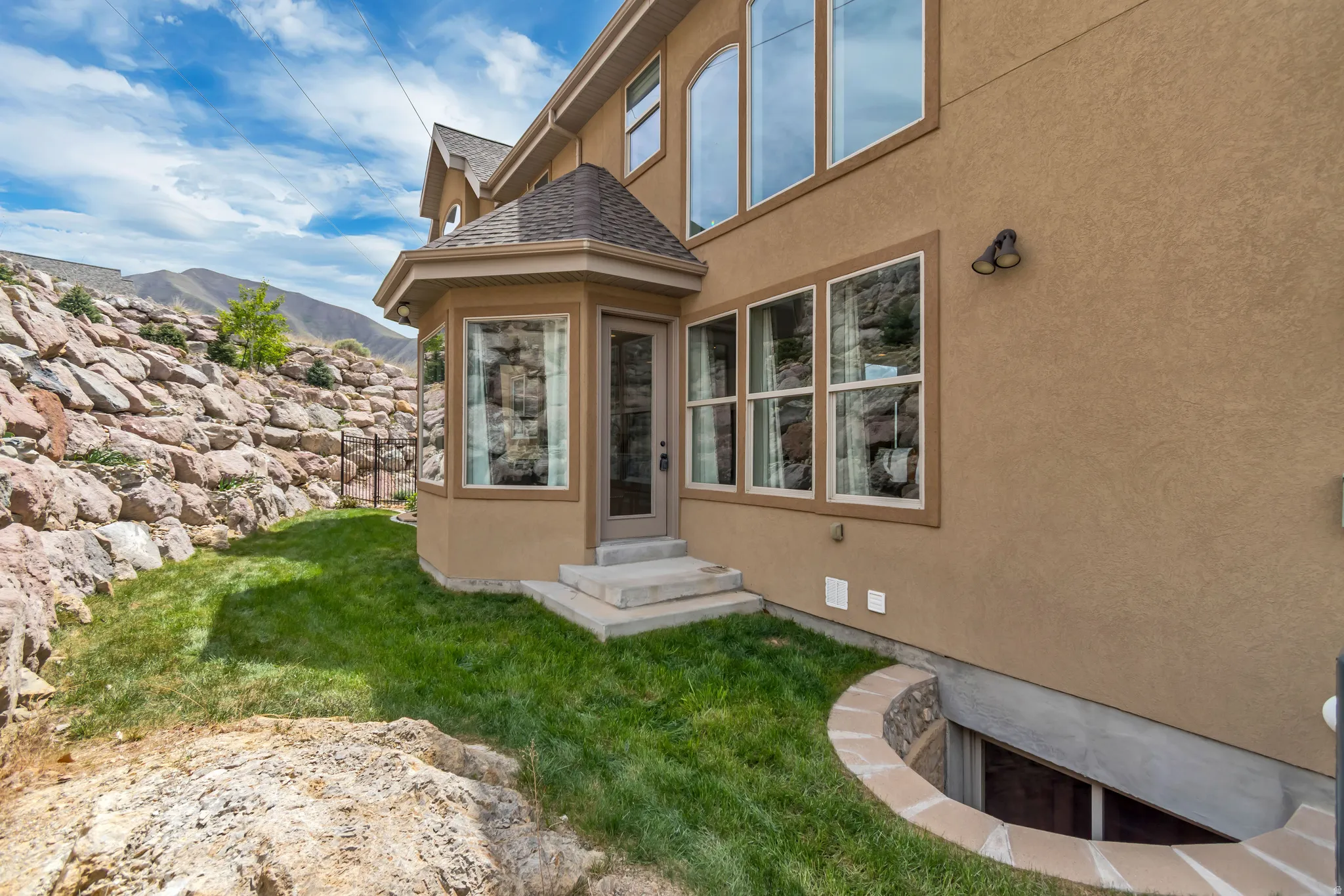View of exterior entry with stucco siding, a lawn, roof with shingles, and a mountain view