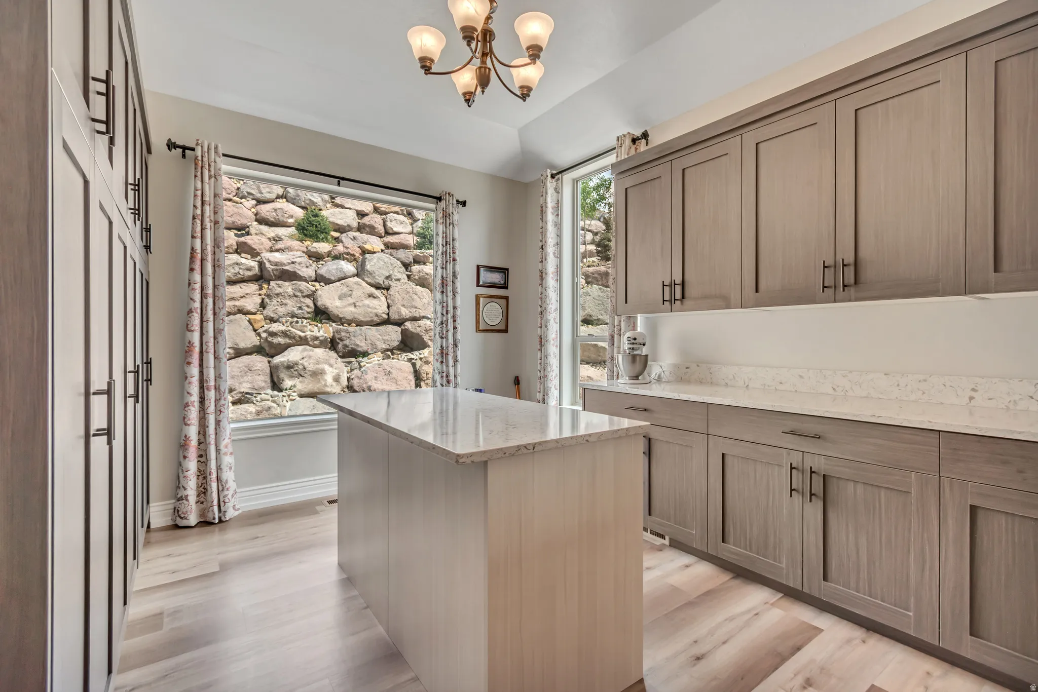 Kitchen with light stone countertops, a kitchen island, light wood finished floors, vaulted ceiling, and hanging lights