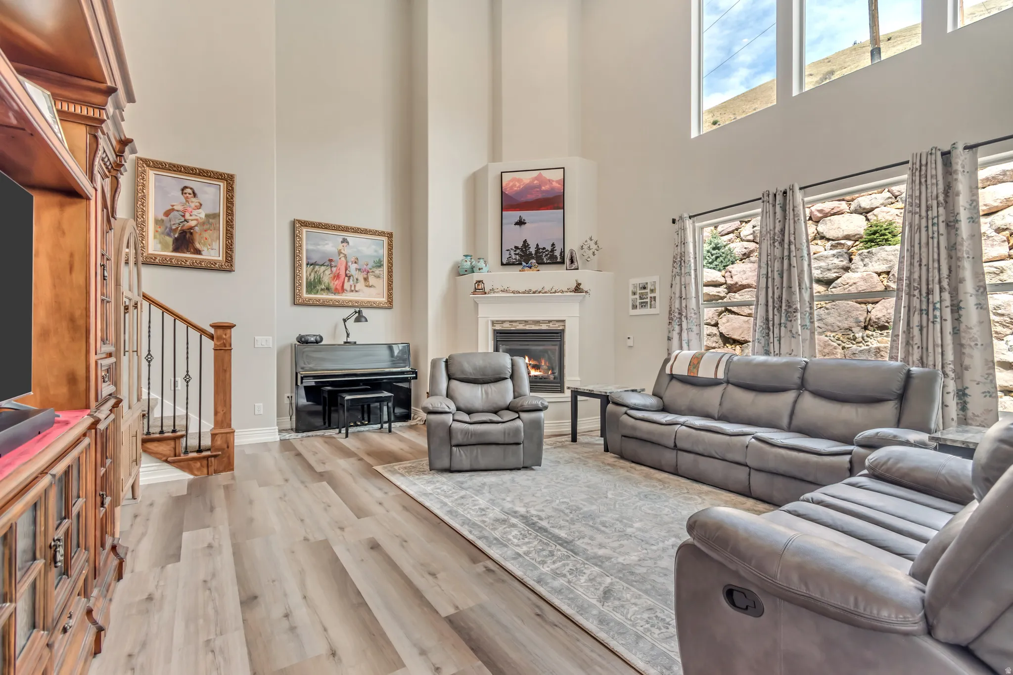 Living room with light wood-type flooring, a glass covered fireplace, a high ceiling, and plenty of natural light