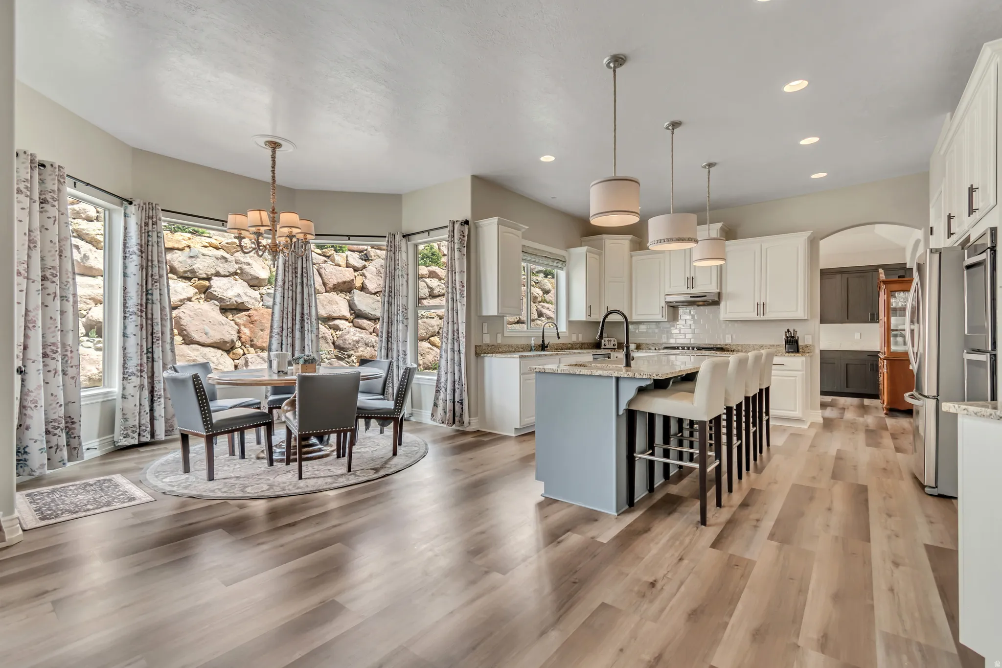 Dual tone kitchen with suspended lighting, a kitchen breakfast bar, light stone counters, an island with sink, and arched walkways
