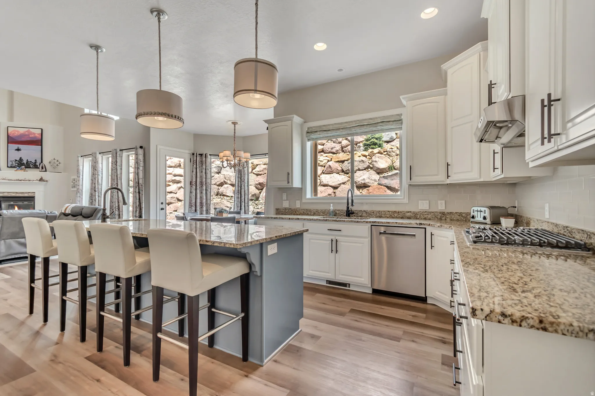 Two tone kitchen featuring a kitchen bar, a center island with sink, light stone counters, open floor plan, and light wood-style flooring