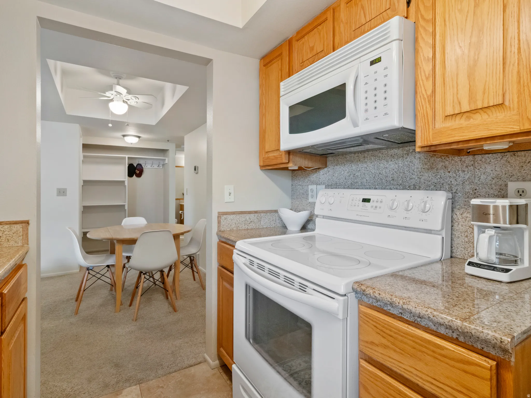 Kitchen featuring white appliances, a tray ceiling, tile counters, backsplash, and a ceiling fan