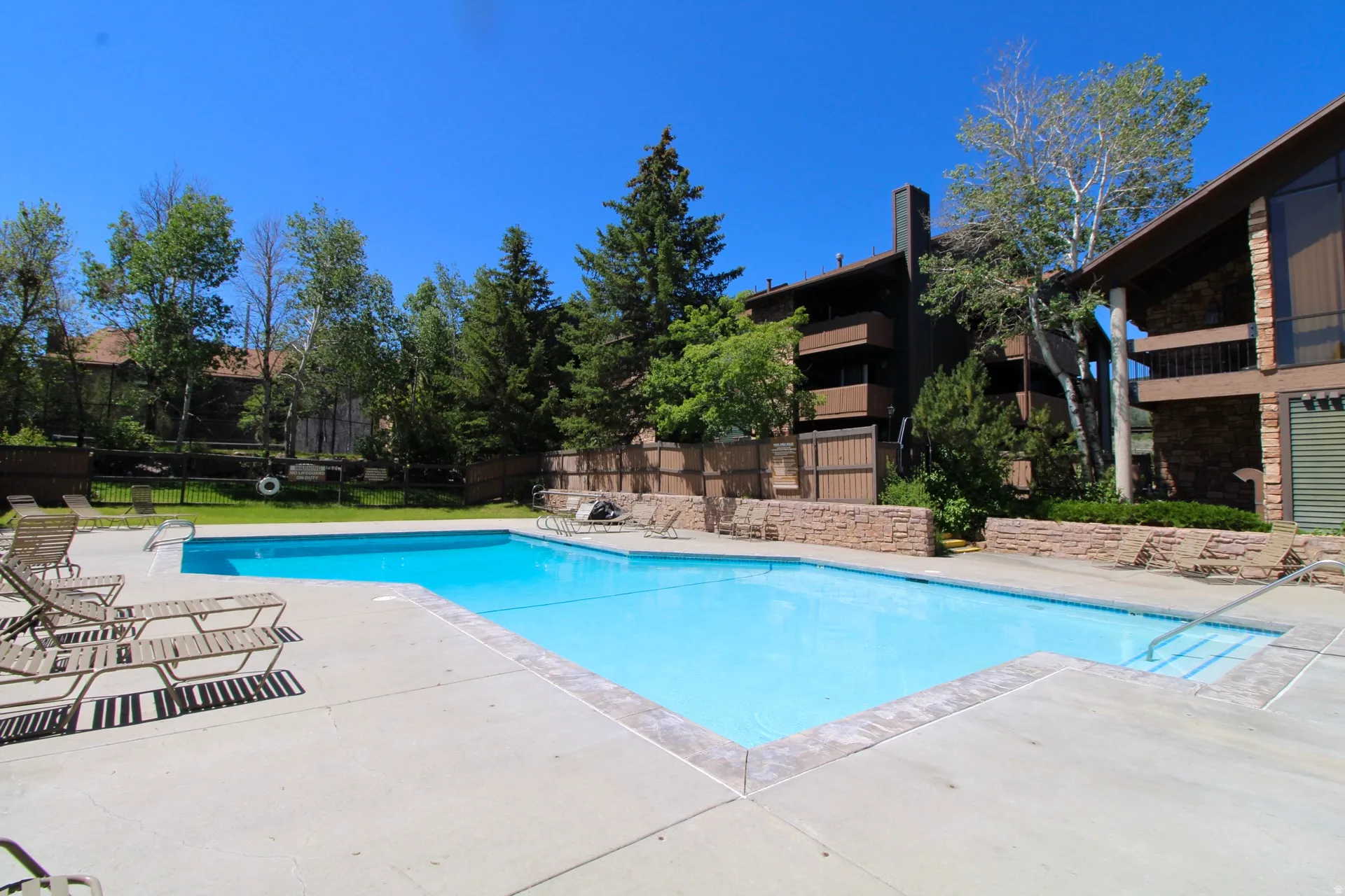 Outdoor swimming pool with concrete decking, surrounded by a stone-capped fence and mature trees