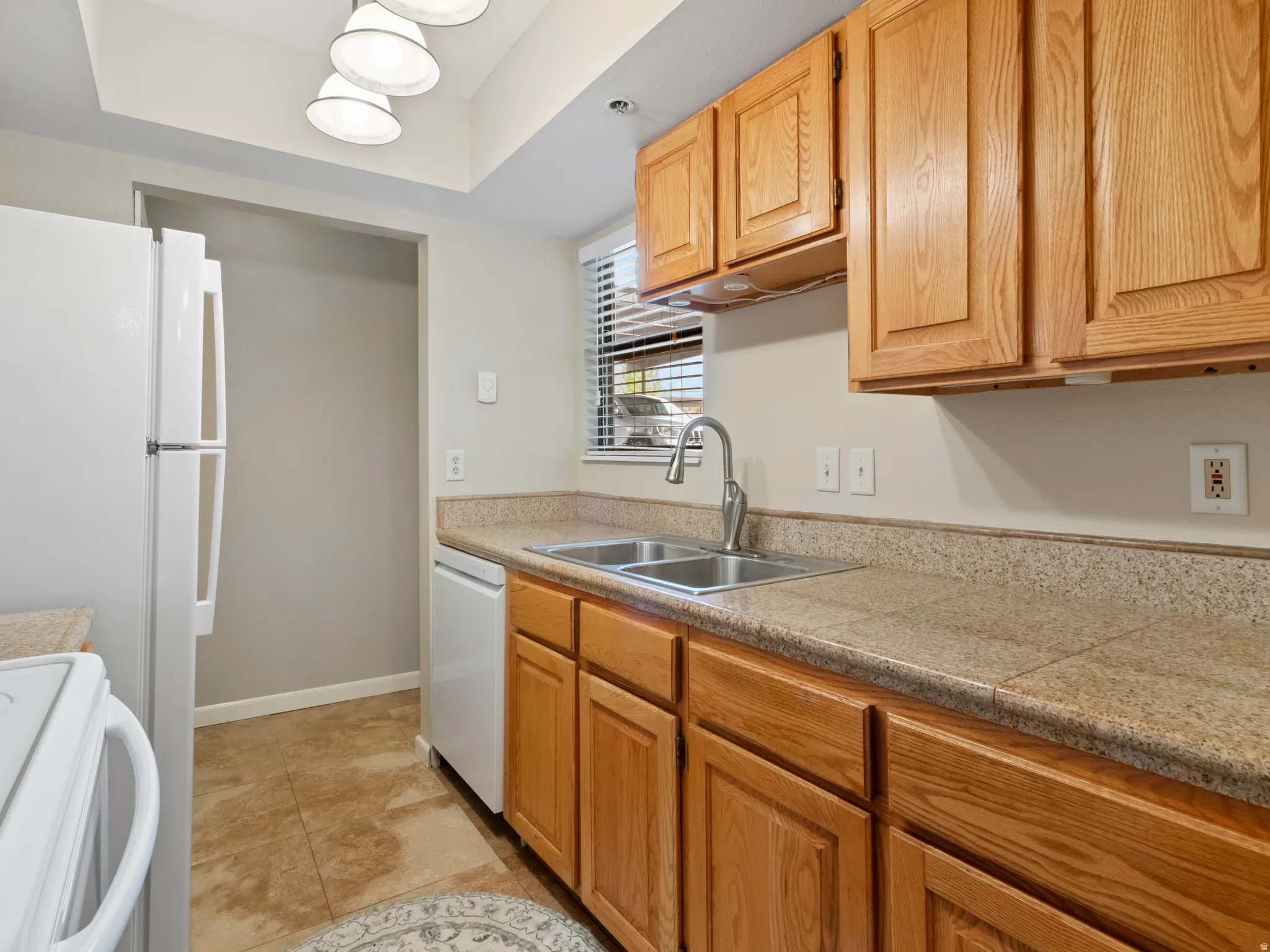 Kitchen with white appliances, tile countertops, a raised ceiling, and light tile patterned flooring
