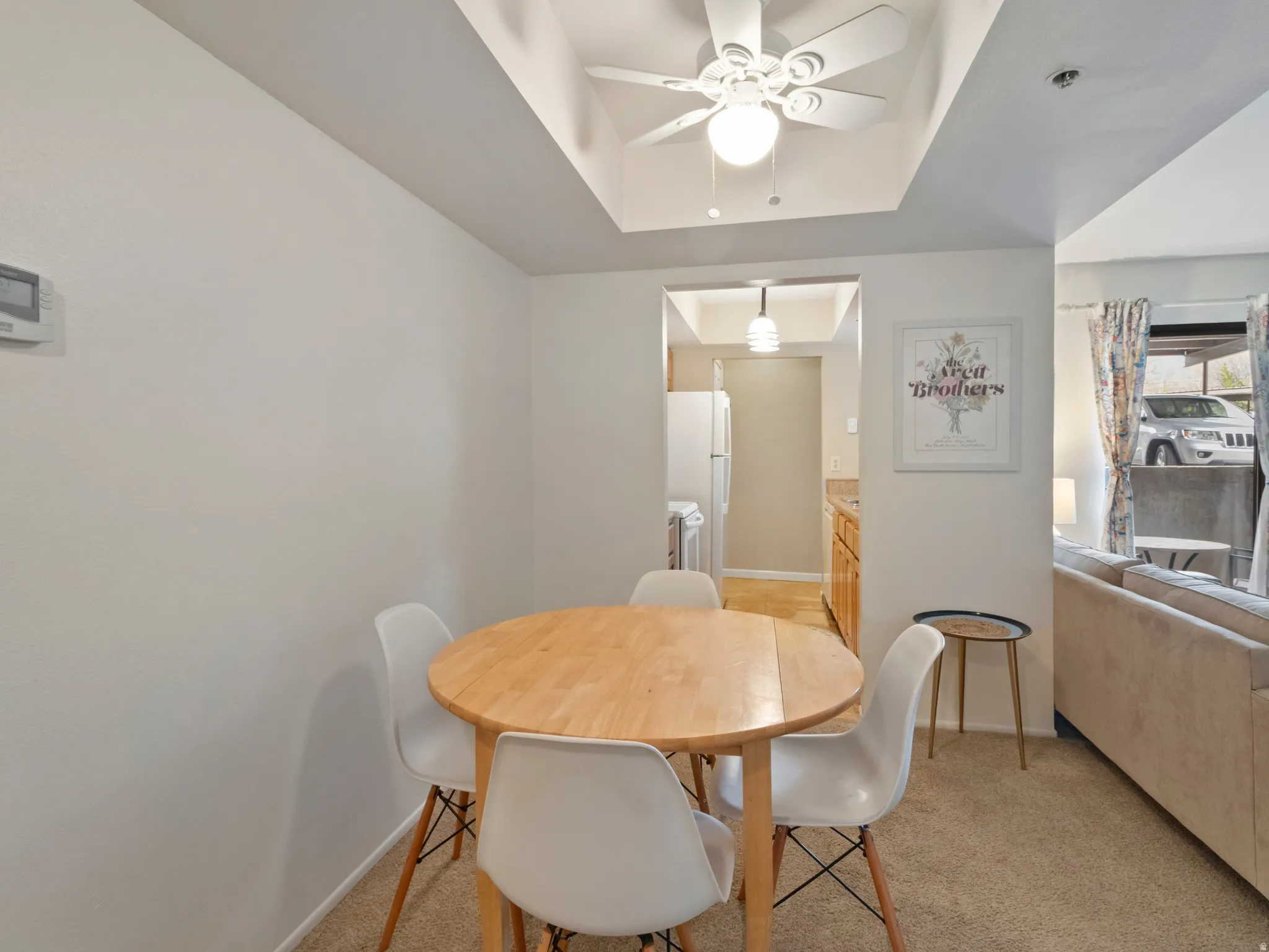 Dining area featuring light colored carpet, a ceiling fan, and a tray ceiling