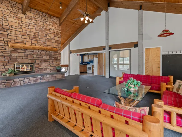 Living room with carpet, a stone fireplace, a high wooden beamed ceiling, and ceiling fan
