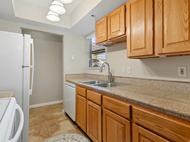 Kitchen with white appliances, tile countertops, a raised ceiling, and light tile patterned flooring