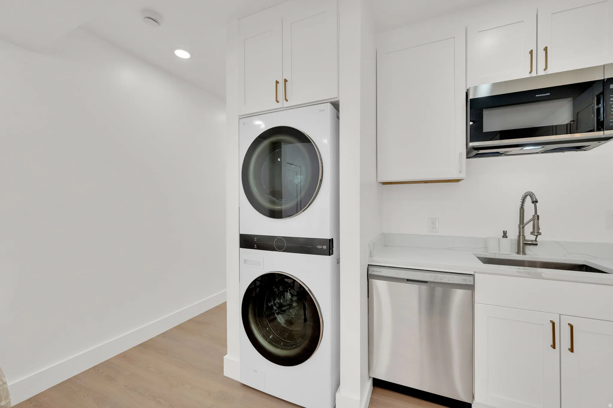 Laundry area with stacked washer and clothes dryer, light wood-type flooring, and recessed lighting