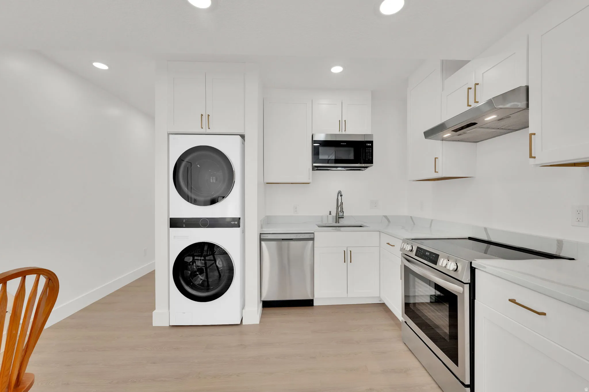 Kitchen featuring stainless steel appliances, white cabinetry, light wood-type flooring, recessed lighting, and light stone countertops