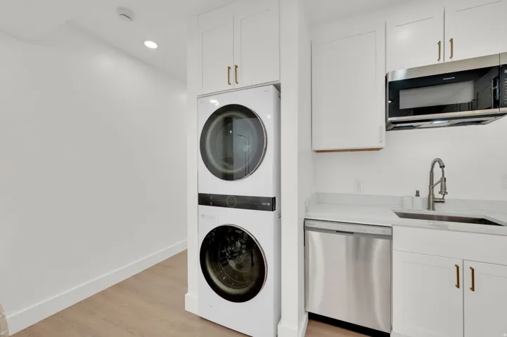 Laundry area with stacked washer and clothes dryer, light wood-type flooring, and recessed lighting