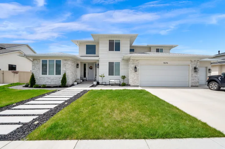 Traditional home featuring a garage, concrete driveway, stone siding, and a front lawn
