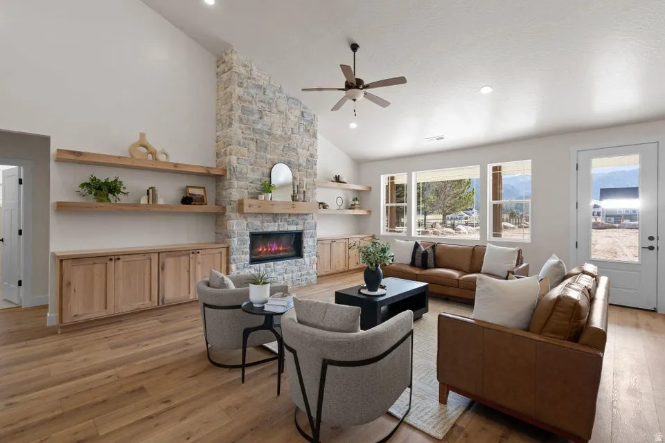 Living room with vaulted ceiling, light wood finished floors, ceiling fan, a stone fireplace, and recessed lighting