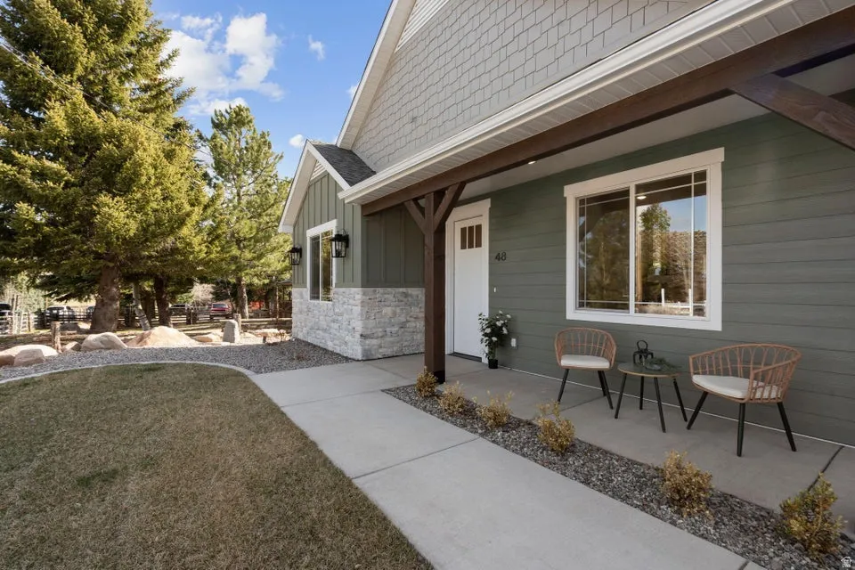 View of exterior entry with a yard, roof with shingles, board and batten siding, stone siding, and covered porch