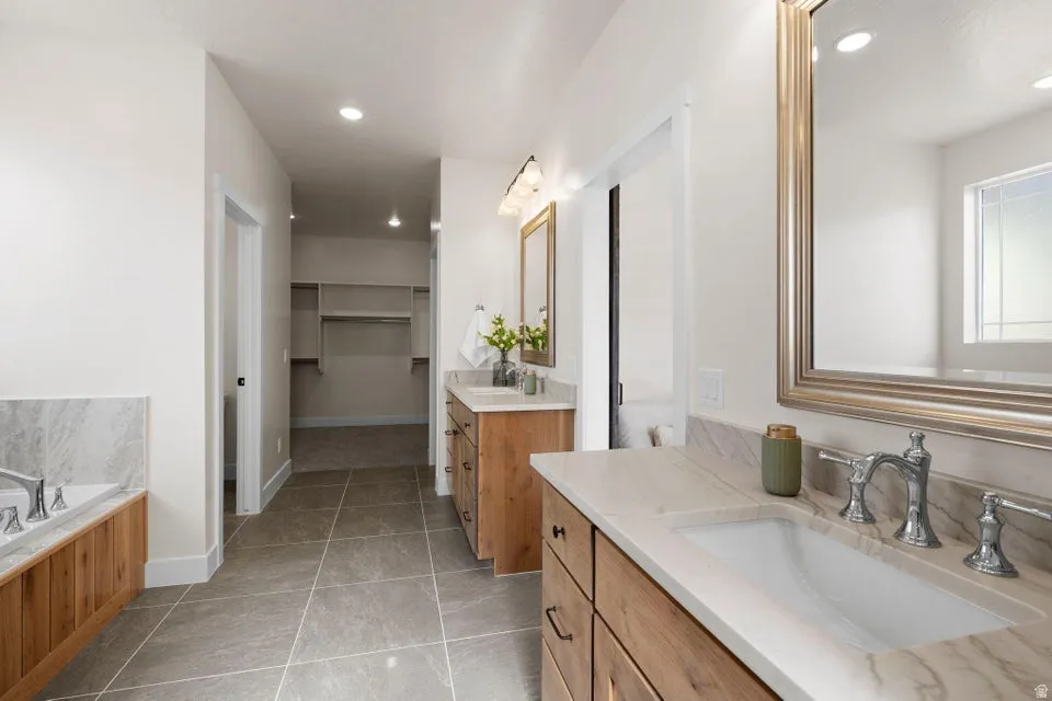 Bathroom featuring two vanities, a spacious closet, a bath, and recessed lighting