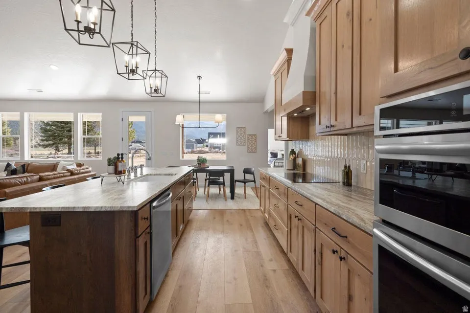 Kitchen featuring a breakfast bar, light stone counters, stainless steel appliances, light wood-style floors, and an island with sink