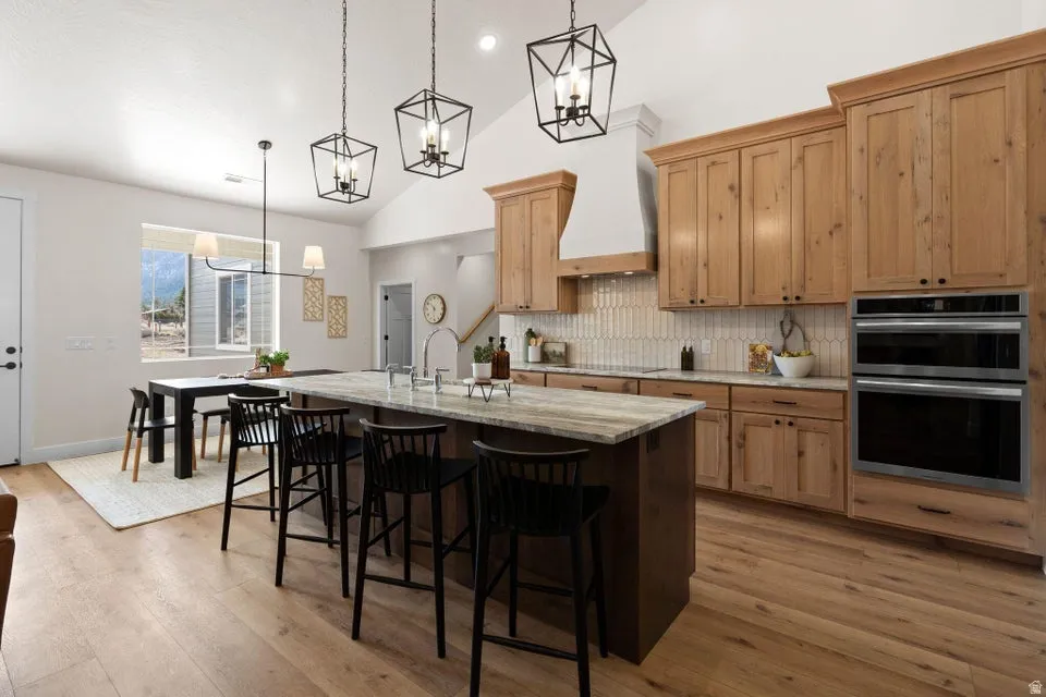 Kitchen featuring vaulted ceiling, light stone counters, suspended lighting, a breakfast bar, and a kitchen island with sink