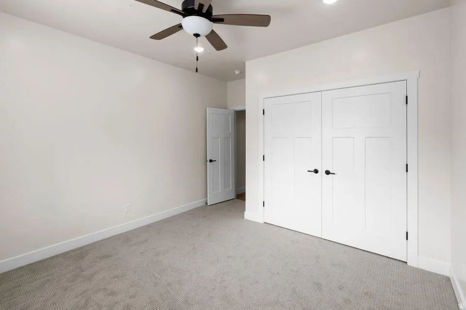 Unfurnished bedroom featuring light carpet, a closet, and ceiling fan