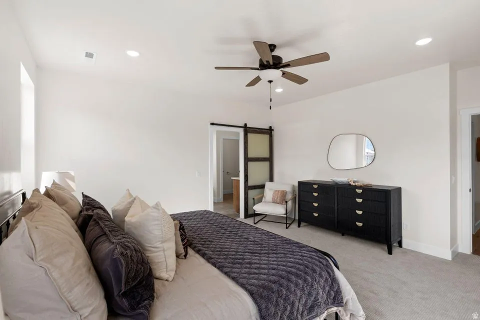 Carpeted bedroom featuring a barn door, ceiling fan, and recessed lighting