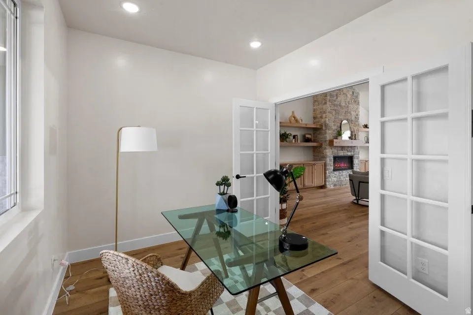 Office space featuring a stone fireplace, wood finished floors, french doors, and recessed lighting
