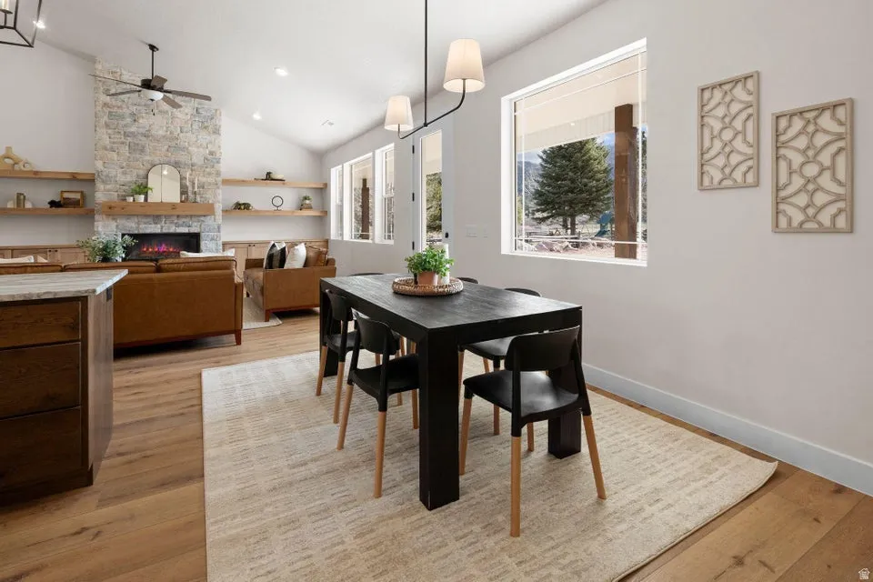 Dining room with a stone fireplace, vaulted ceiling, light wood-type flooring, and ceiling fan