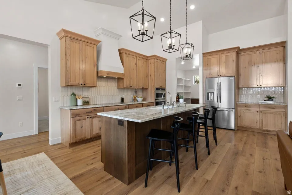 Kitchen featuring stainless steel fridge with ice dispenser, light stone countertops, backsplash, a chandelier, and a breakfast bar area