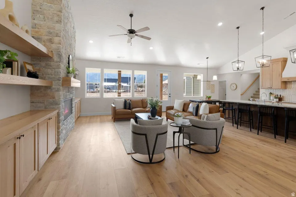Living area featuring a ceiling fan, a stone fireplace, light wood-style flooring, and lofted ceiling