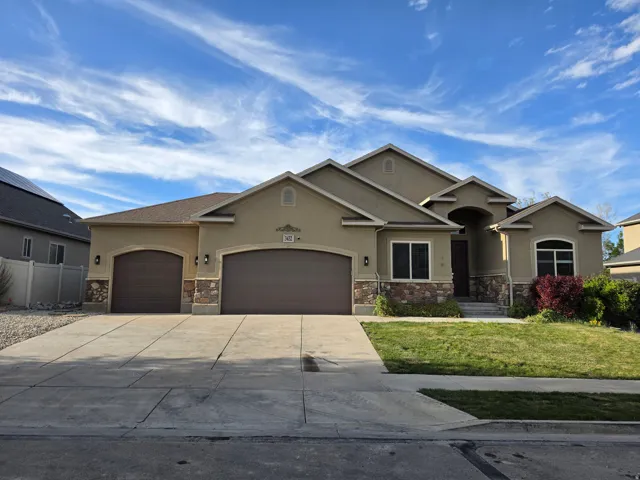 View of front of house with stucco siding, an attached garage, stone siding, concrete driveway, and a front lawn