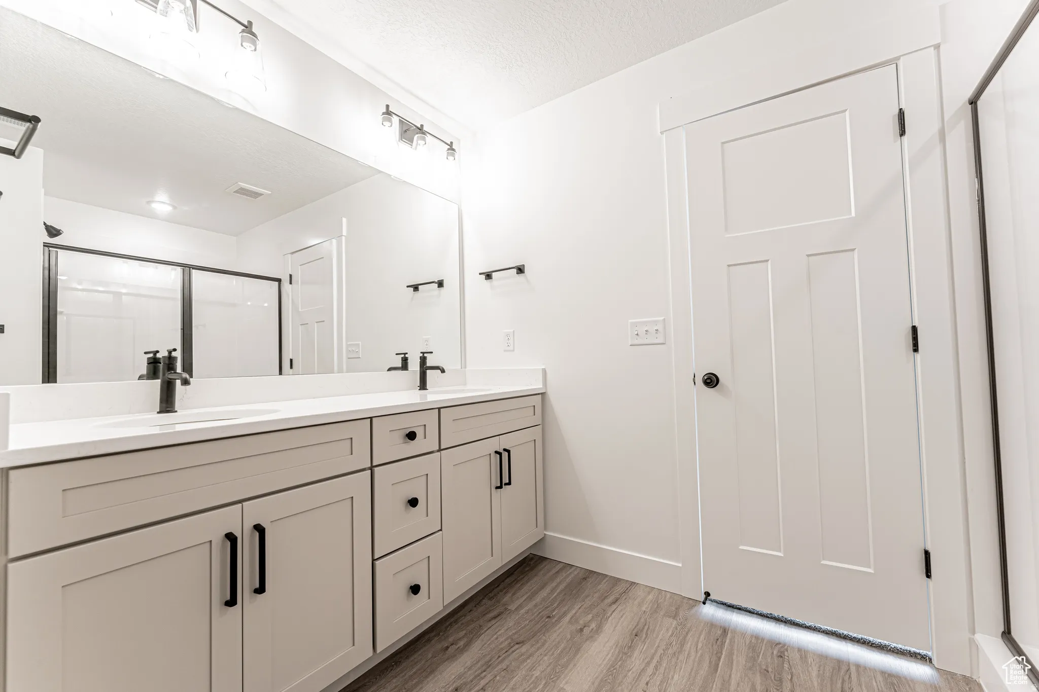 Full bathroom with double vanity, a shower stall, light wood-type flooring, and a textured ceiling