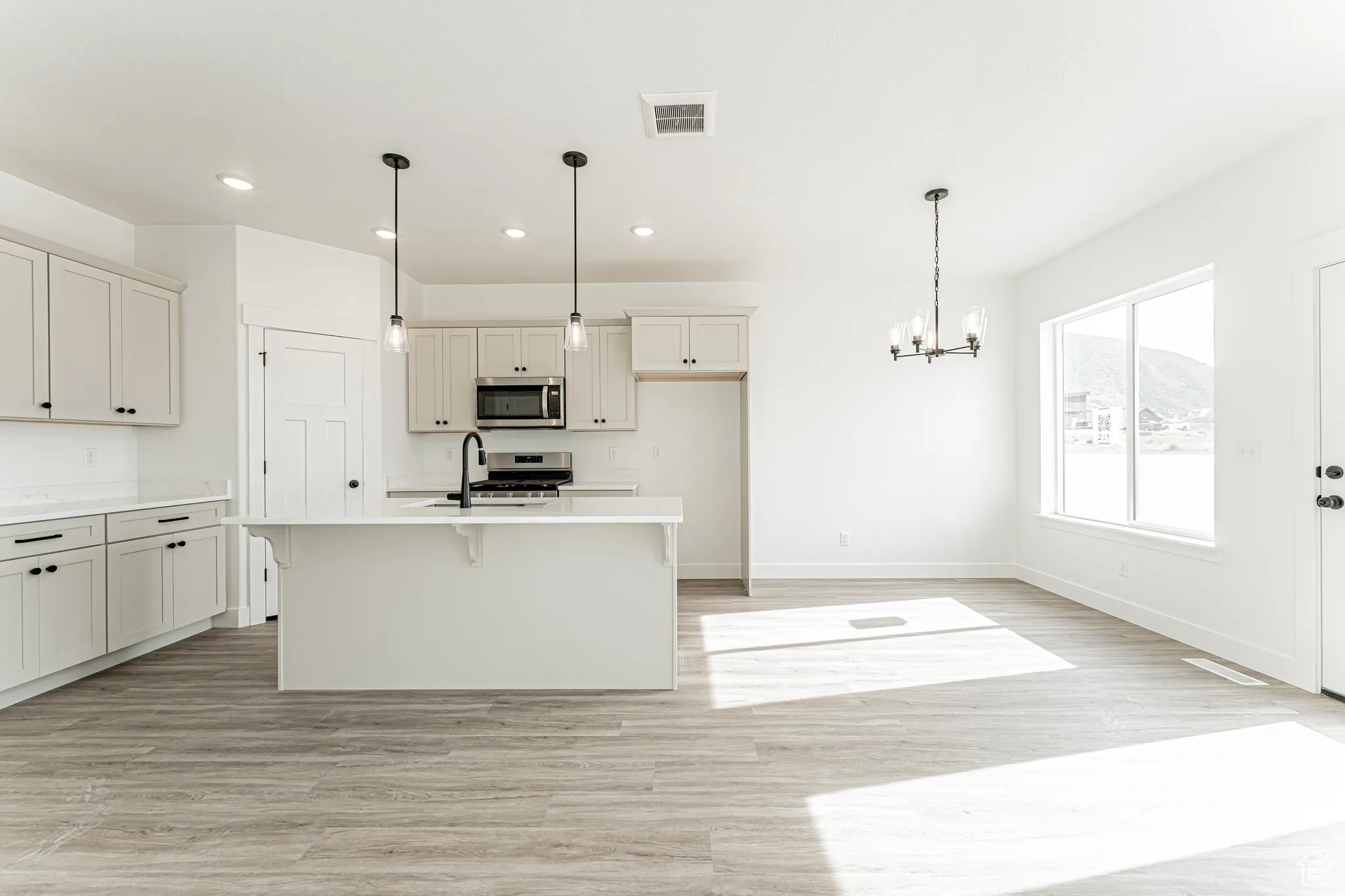 Kitchen with hanging lights, light wood-type flooring, a kitchen breakfast bar, stainless steel appliances, and light stone counters