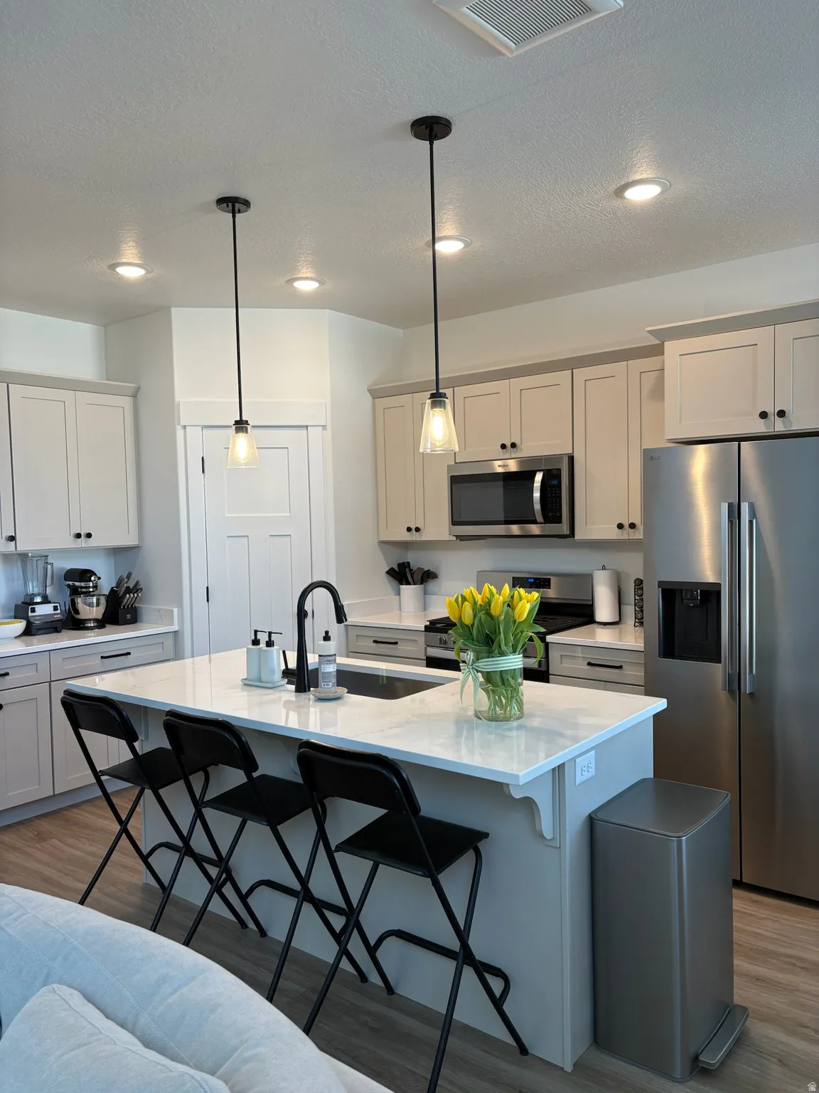 Kitchen with stainless steel appliances, light wood-style floors, a kitchen bar, an island with sink, and a textured ceiling