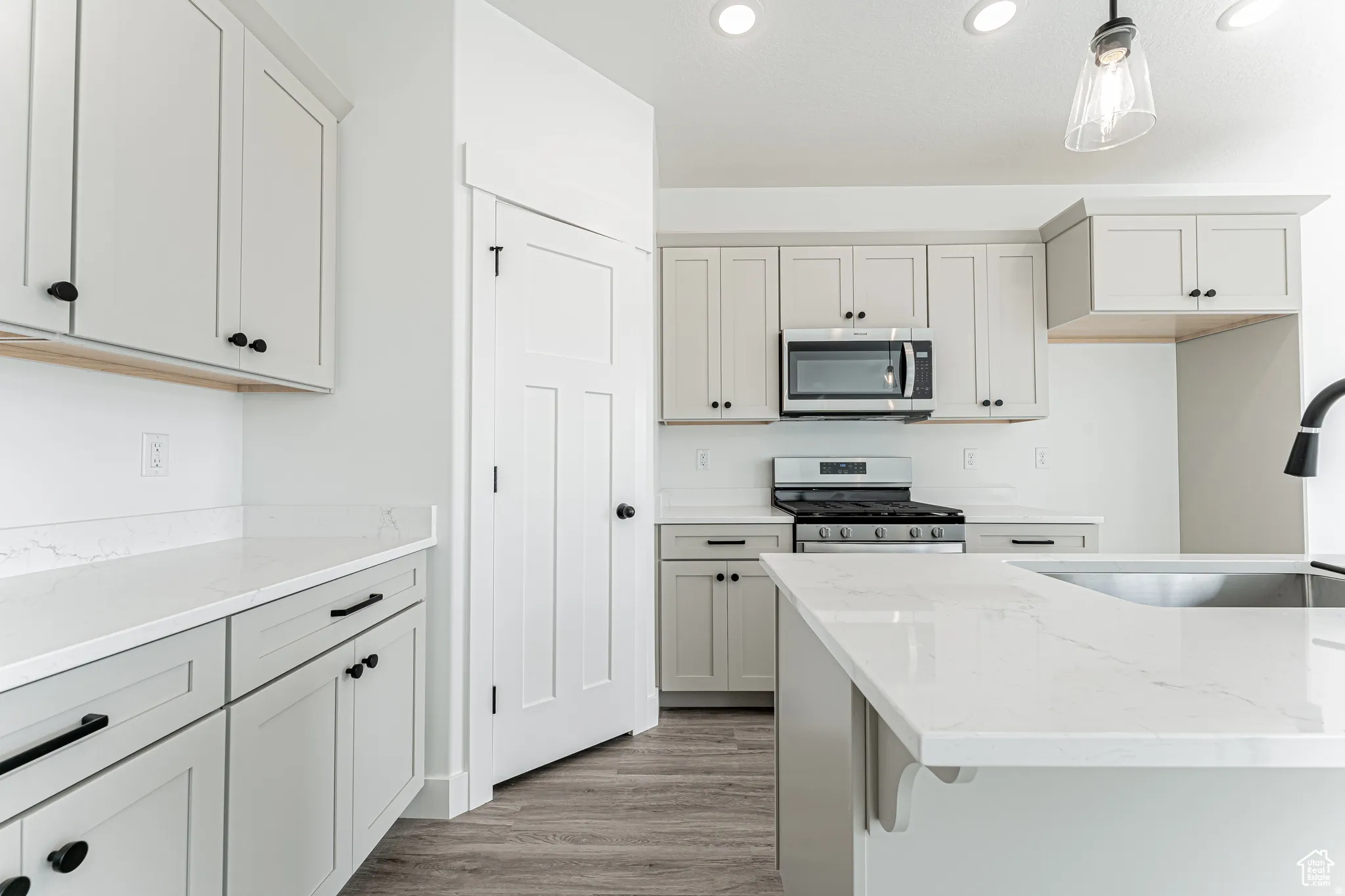 Kitchen featuring light stone countertops, stainless steel appliances, light wood finished floors, and hanging light fixtures
