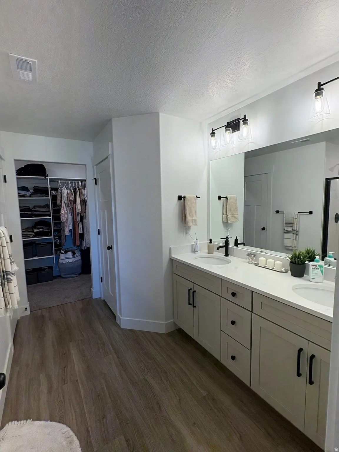 Bathroom featuring double vanity, a walk in closet, a textured ceiling, dark wood finished floors, and a shower stall
