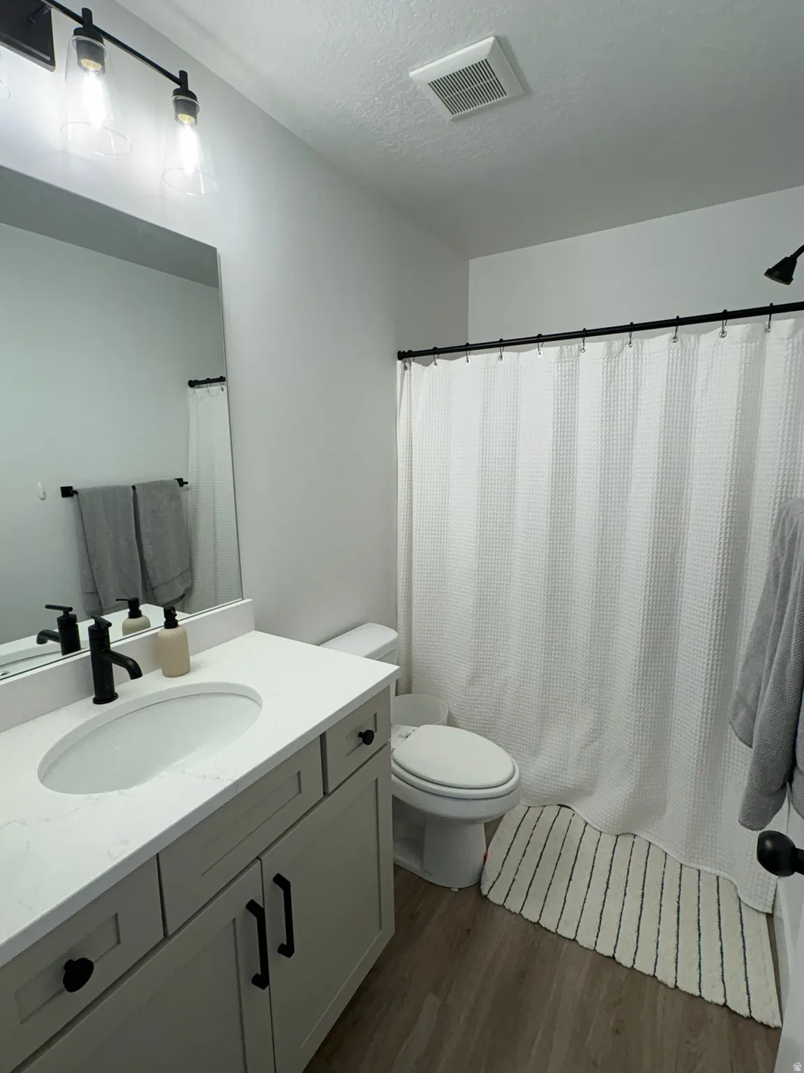 Bathroom with vanity, dark wood-style floors, a shower with curtain, and a textured ceiling
