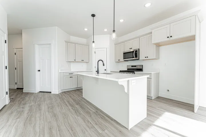 Kitchen featuring a breakfast bar, stainless steel appliances, light wood-style flooring, pendant lighting, and a center island with sink