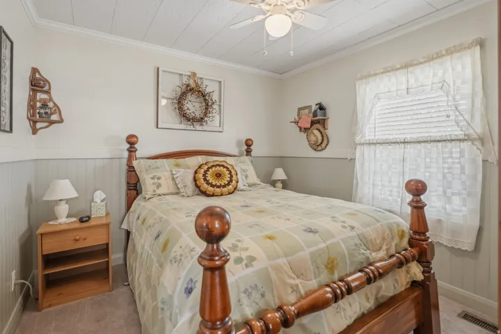 Bedroom featuring crown molding, a wainscoted wall, a ceiling fan, and carpet floors