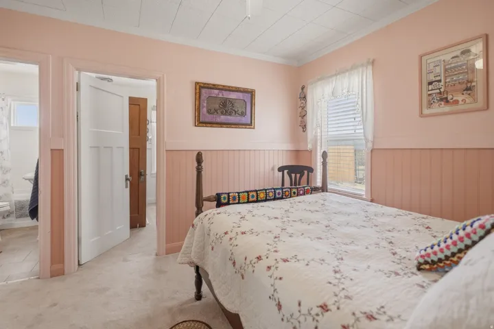 Bedroom with wainscoting, crown molding, light carpet, and connected bathroom