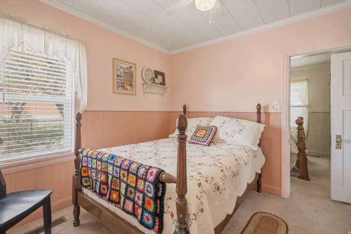 Bedroom with a wainscoted wall, ornamental molding, a ceiling fan, and light colored carpet