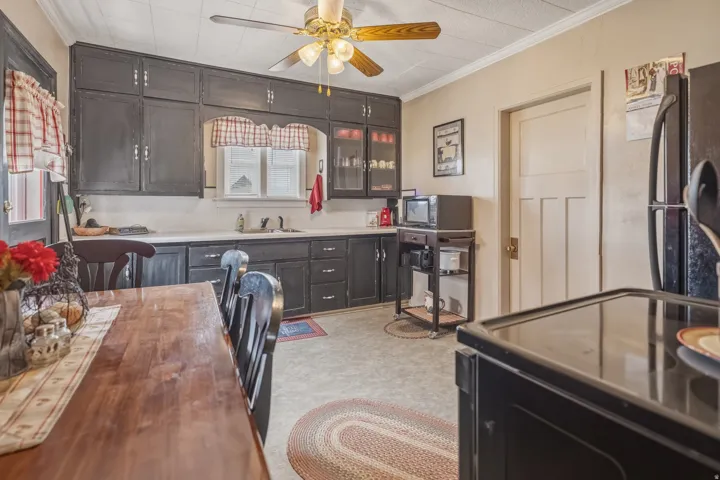 Kitchen with black appliances, crown molding, a ceiling fan, glass fronted cabinets, and light floors
