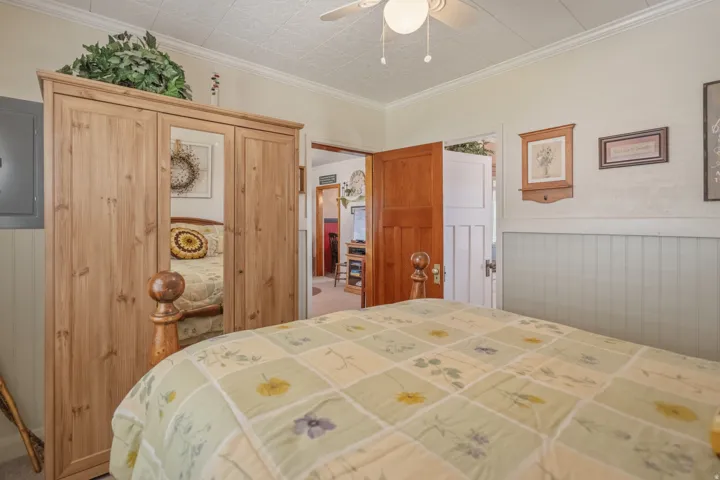 Bedroom with a closet, electric panel, wainscoting, crown molding, and a ceiling fan