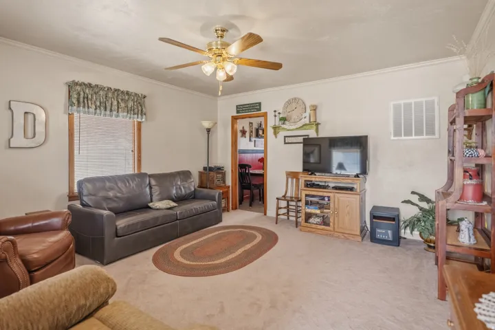 Living area featuring light carpet, ornamental molding, and a ceiling fan