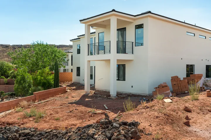 Contemporary stucco exterior featuring a second-story balcony with black metal railings, dark-framed windows, and a flat roofline